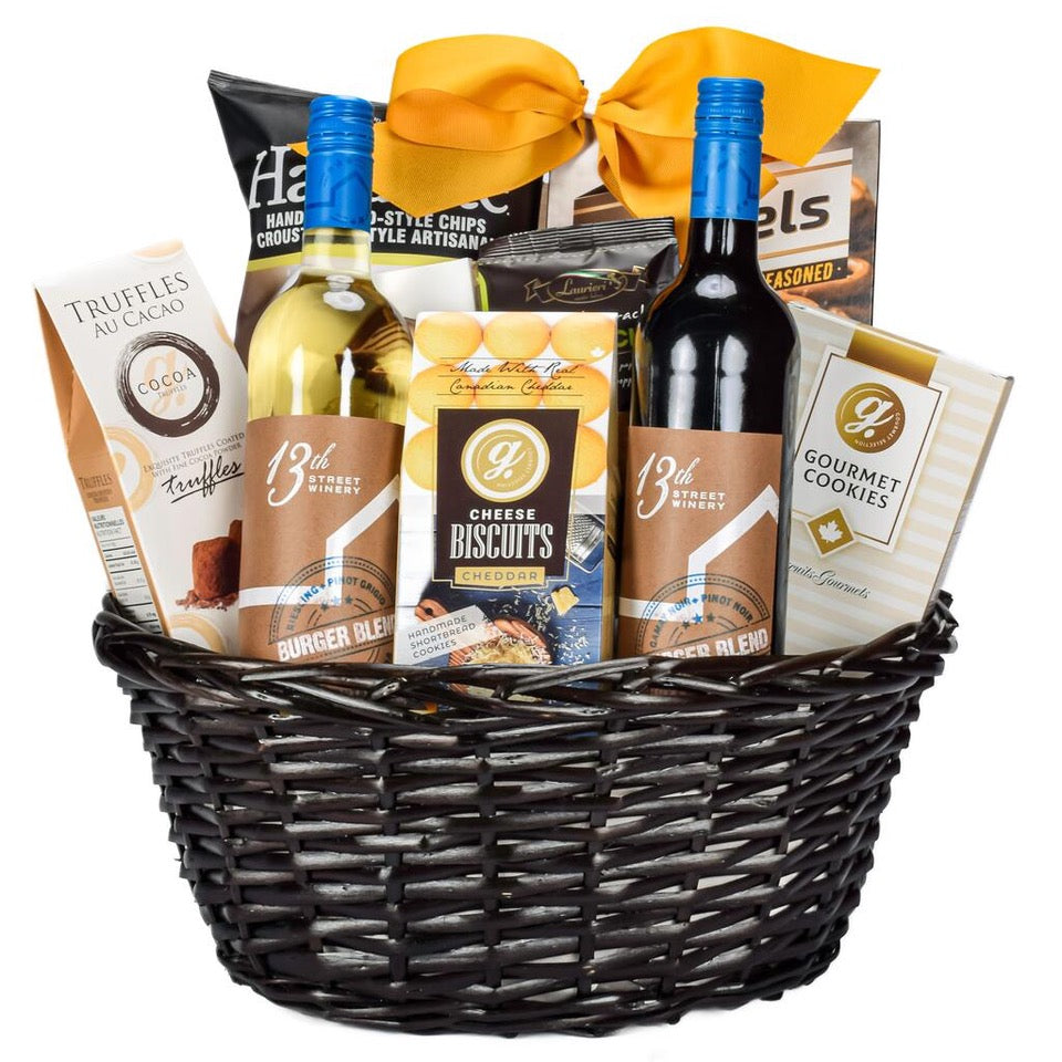 Canadian Red And White Wine With Chips, Pretzels, Truffles, Milk Chocolate, Cheddar Cookies, Shortbread Cookies, And Crackers In A Oval Wicker Basket With A Gold Bow